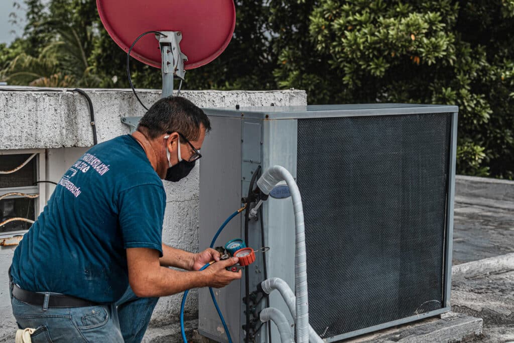 HVAC technician servicing an outdoor air conditioning unit, using gauges to check refrigerant levels.