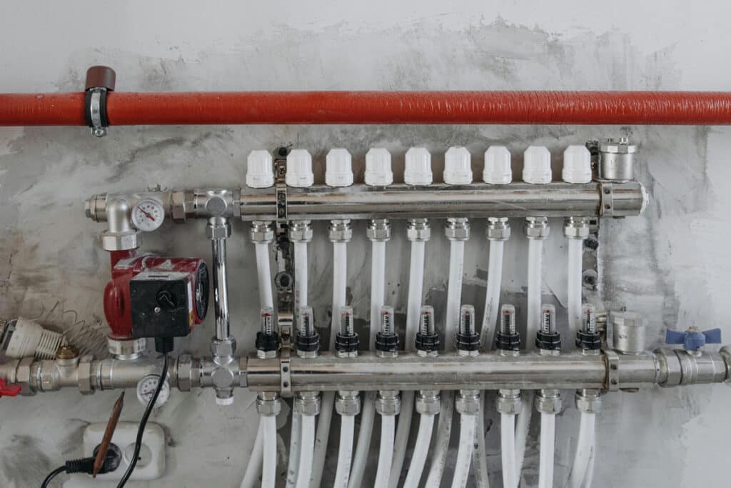 Installed plumbing manifold with white pipes, valves, and gauges mounted on a wall.