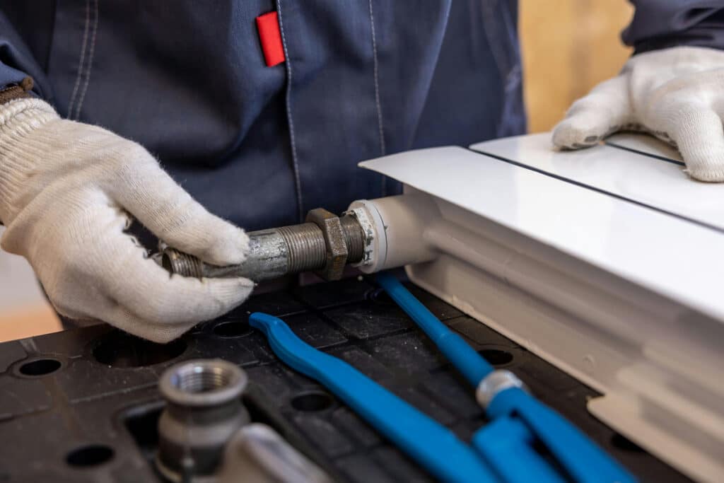 A handyman or plumber working with a metal pipe fitting and tools, performing a service at a job site.
