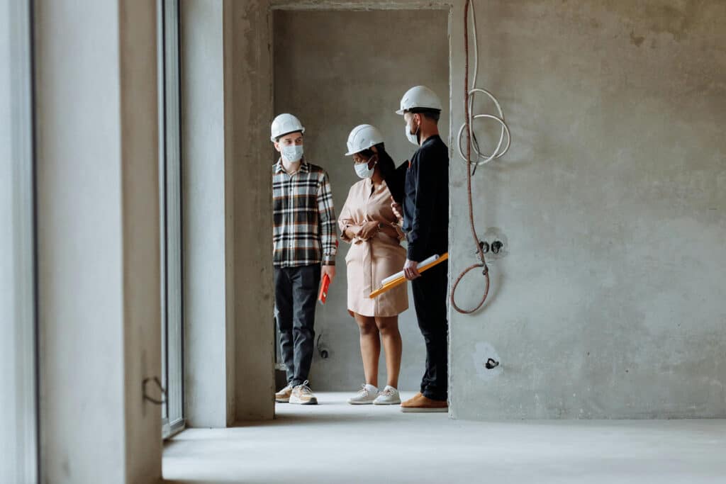 A construction team discusses plans on-site, wearing hard hats, and reviews project details.